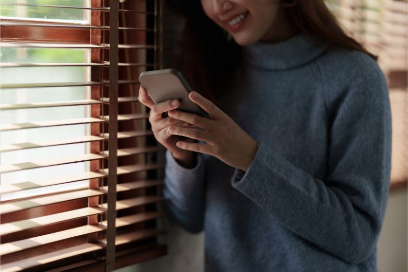 une femme regardant son téléphone portable devant une fenêtre